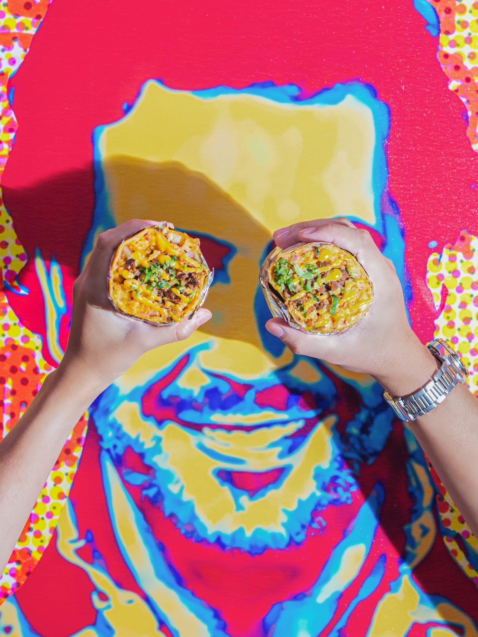 Two Taco J burritos held up against a pop-art wall