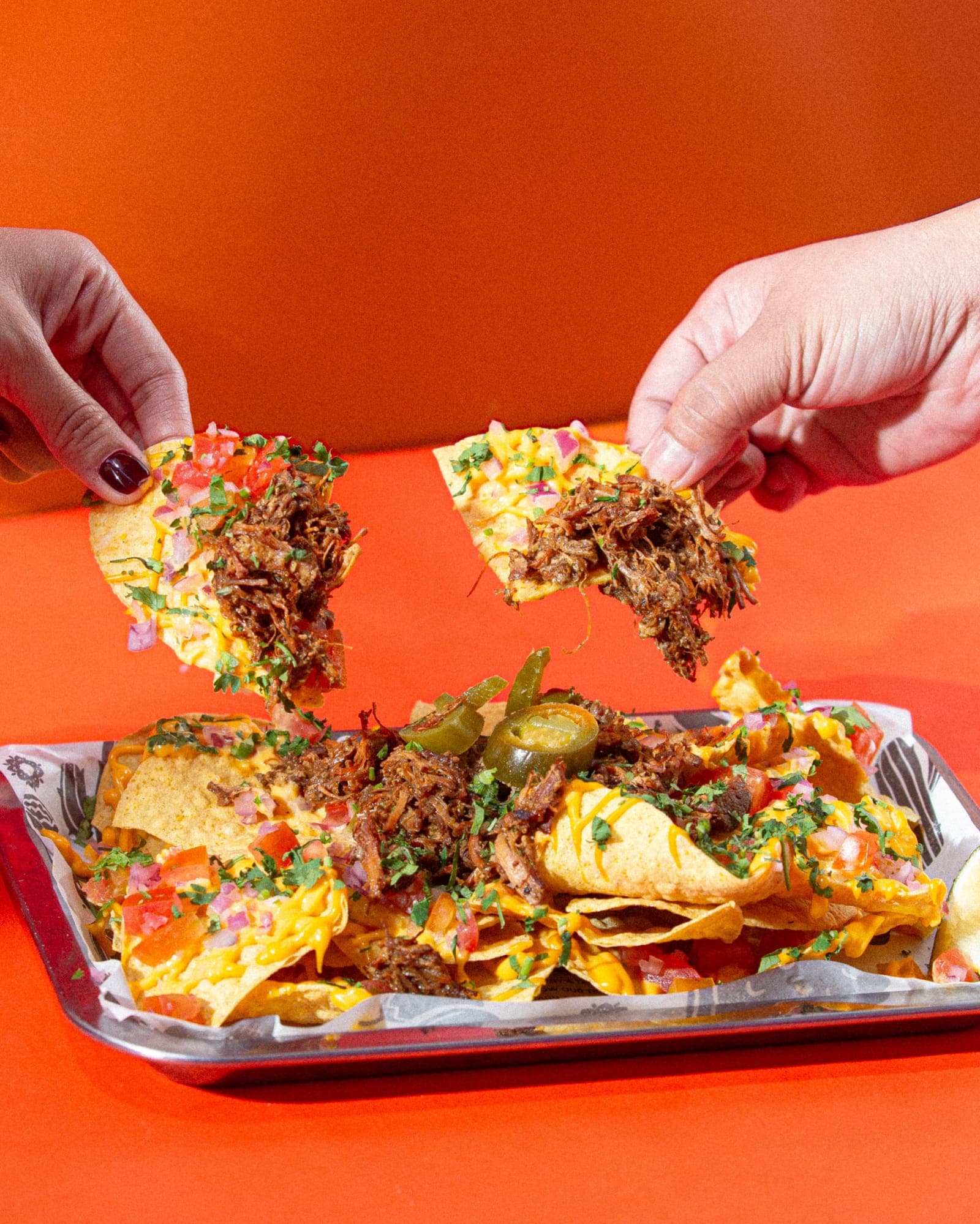 Two hands grabbing loaded nachos from a tray